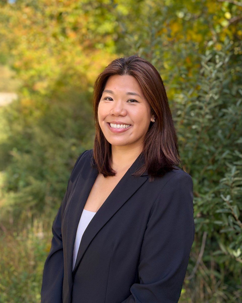 Jennifer Russ smiling in a black blazer in front of autumn greenery